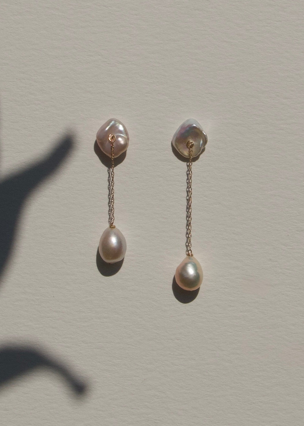 Alba - The top of these earrings features two keshi pearls shaped like conch shells, offering a unique and textured focal point. From each, a delicate rope chain drapes down to light pink baroque pearls, creating a graceful, understated design that highli