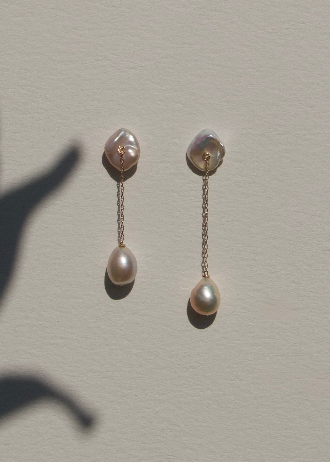 Alba - The top of these earrings features two keshi pearls shaped like conch shells, offering a unique and textured focal point. From each, a delicate rope chain drapes down to light pink baroque pearls, creating a graceful, understated design that highli