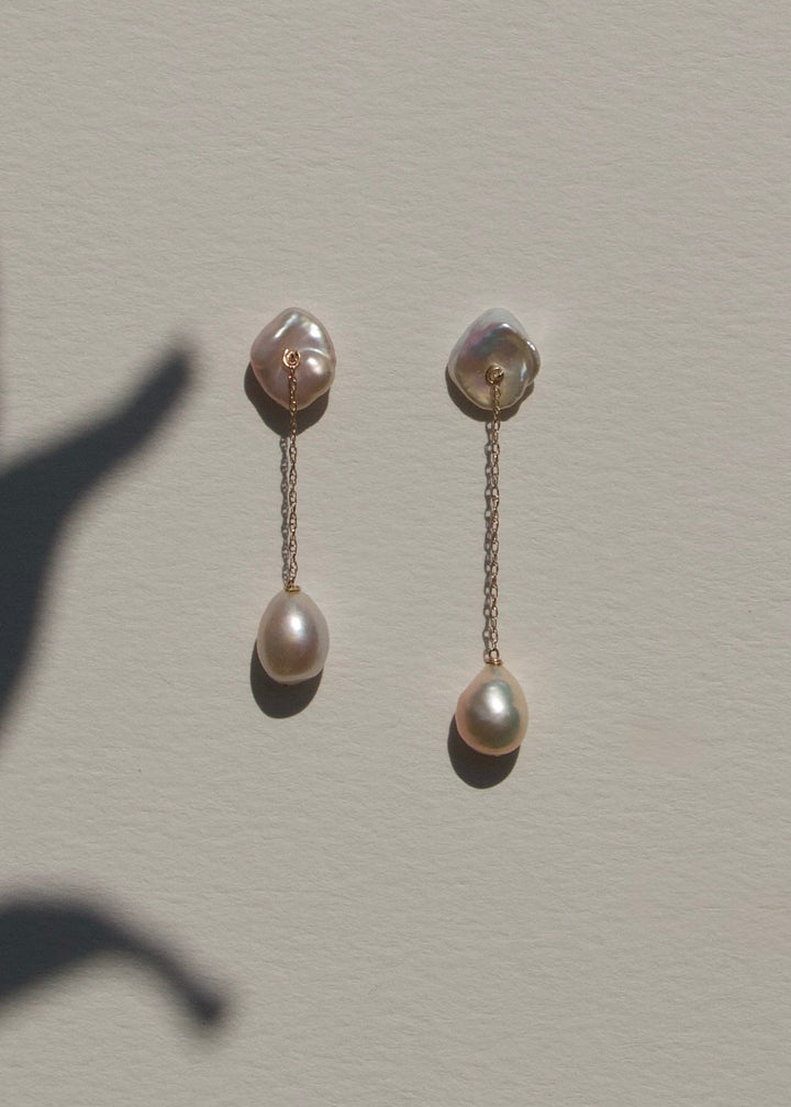 Alba - The top of these earrings features two keshi pearls shaped like conch shells, offering a unique and textured focal point. From each, a delicate rope chain drapes down to light pink baroque pearls, creating a graceful, understated design that highli