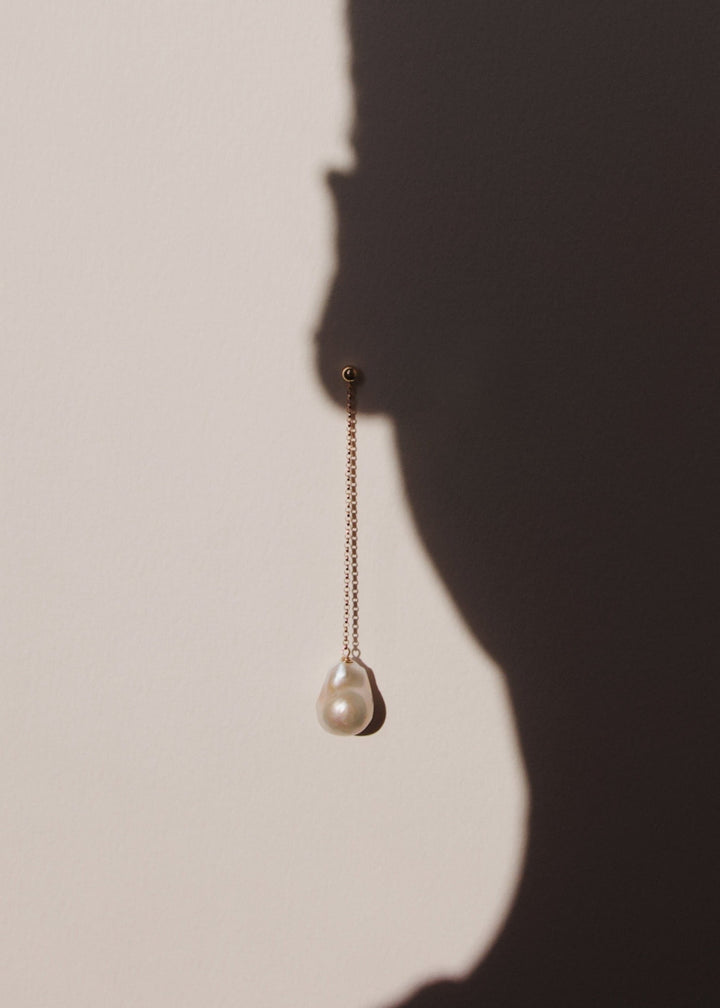 Unique baroque pearl drop earring dangling on a shadow