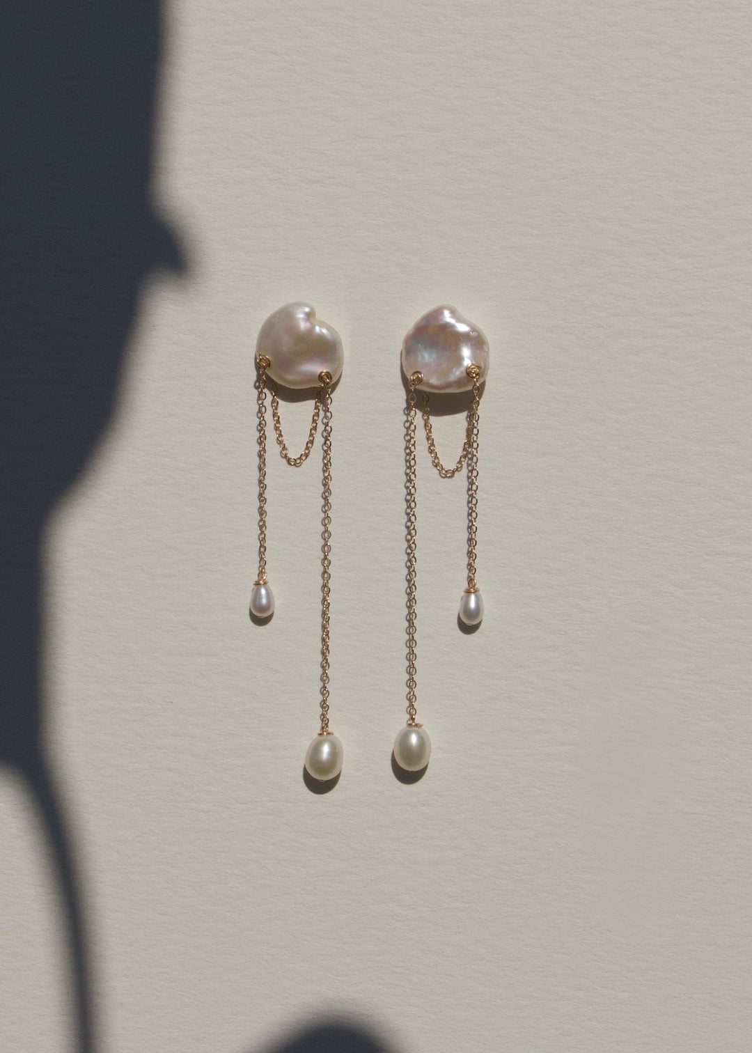 Bria - A single keshi pearl anchors this delicate design, with two fine strands falling at varied lengths. Between them, a single gold chain is draped like a quiet detail you almost missed. Graceful and understated, it’s a perfect choice for a wedding or