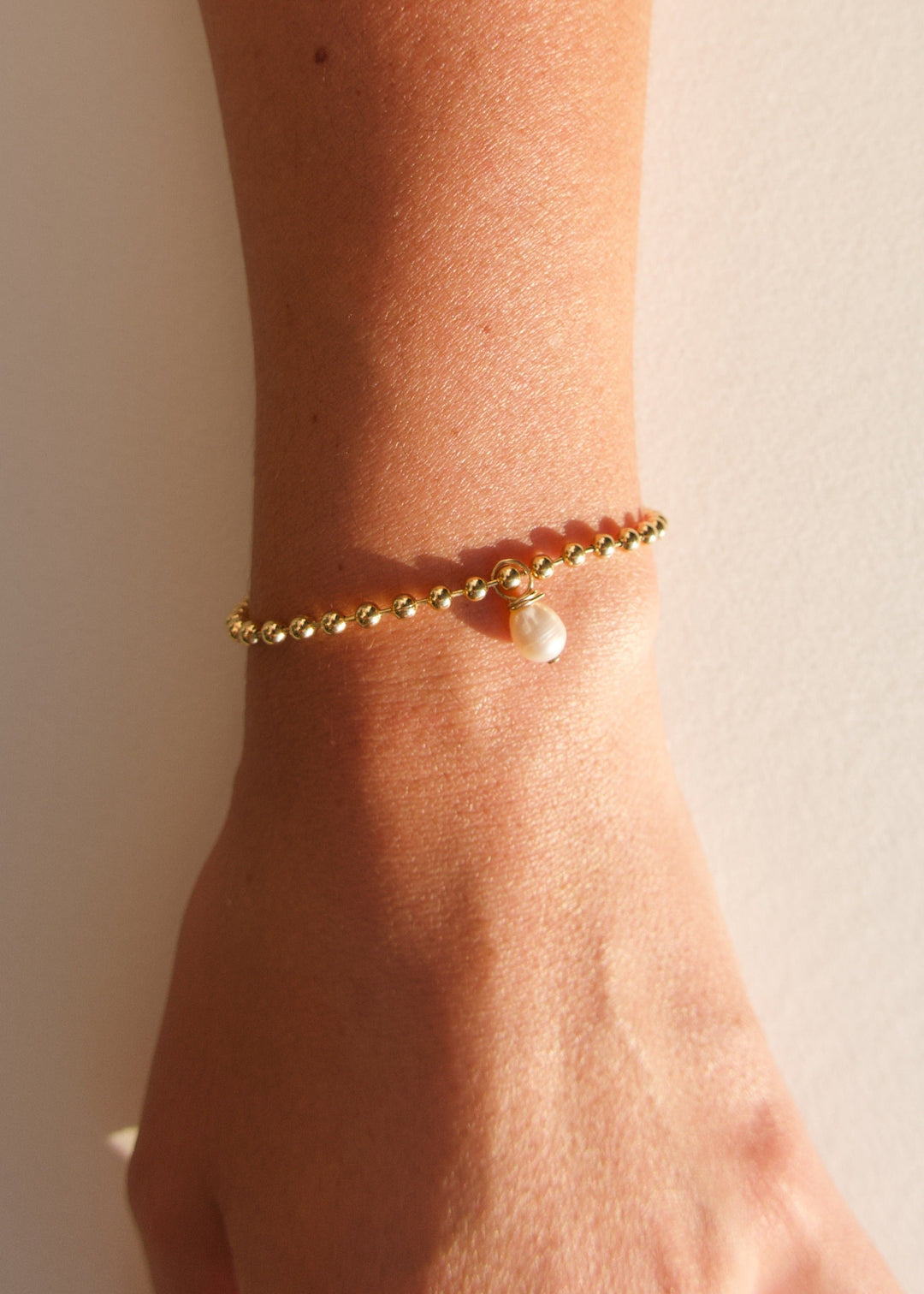 Wearing bracelet adorned with gold beads and a pearl pendant