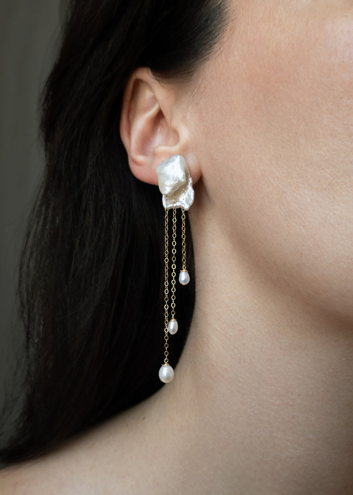 Cleo - Crafted in solid 14k gold, the Cleo earrings feel like wearable sculpture. Two folded keshi pearls create a soft, organic form, each one unique in shape and texture. From their folds, gold chains cascade down, ending in glowing teardrop pearls that