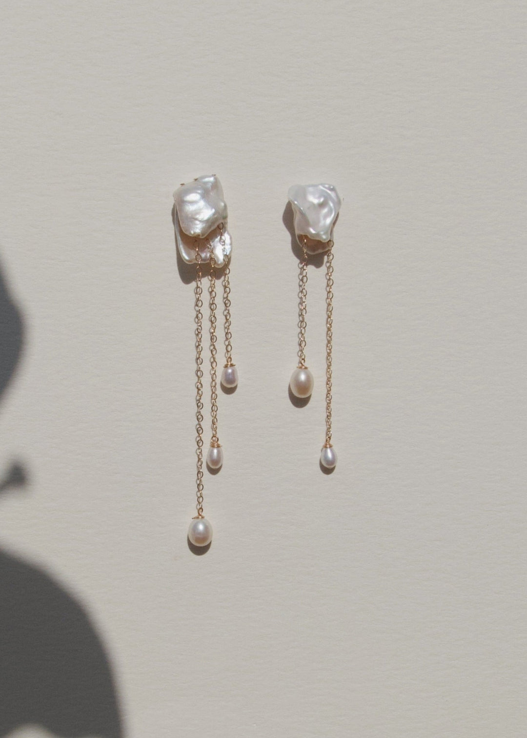 Cleo - Crafted in solid 14k gold, the Cleo earrings feel like wearable sculpture. Two folded keshi pearls create a soft, organic form, each one unique in shape and texture. From their folds, gold chains cascade down, ending in glowing teardrop pearls that