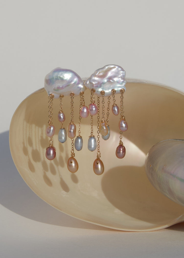 Daydream 14k gold earrings with white keshi pearl tops and multicolored teardrop pearls on dangling chains, displayed on a shell.