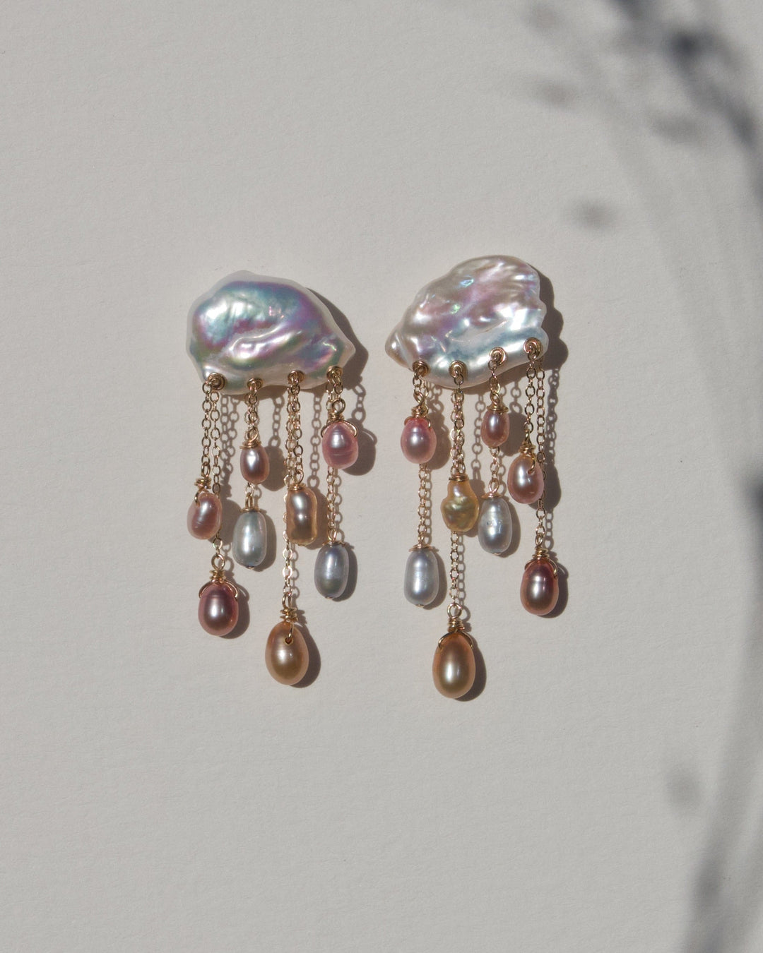 Daydream keshi pearl earrings with multicolored teardrop pearls suspended from 14k gold chains, styled with botanical shadows.