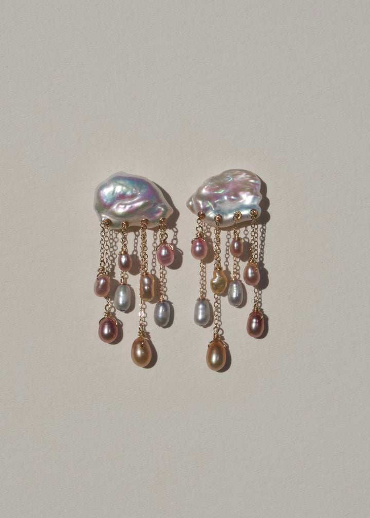 Pair of Daydream 14k gold earrings with white keshi pearl tops and pink, peach and silvery teardrop pearls on chains against a neutral background.