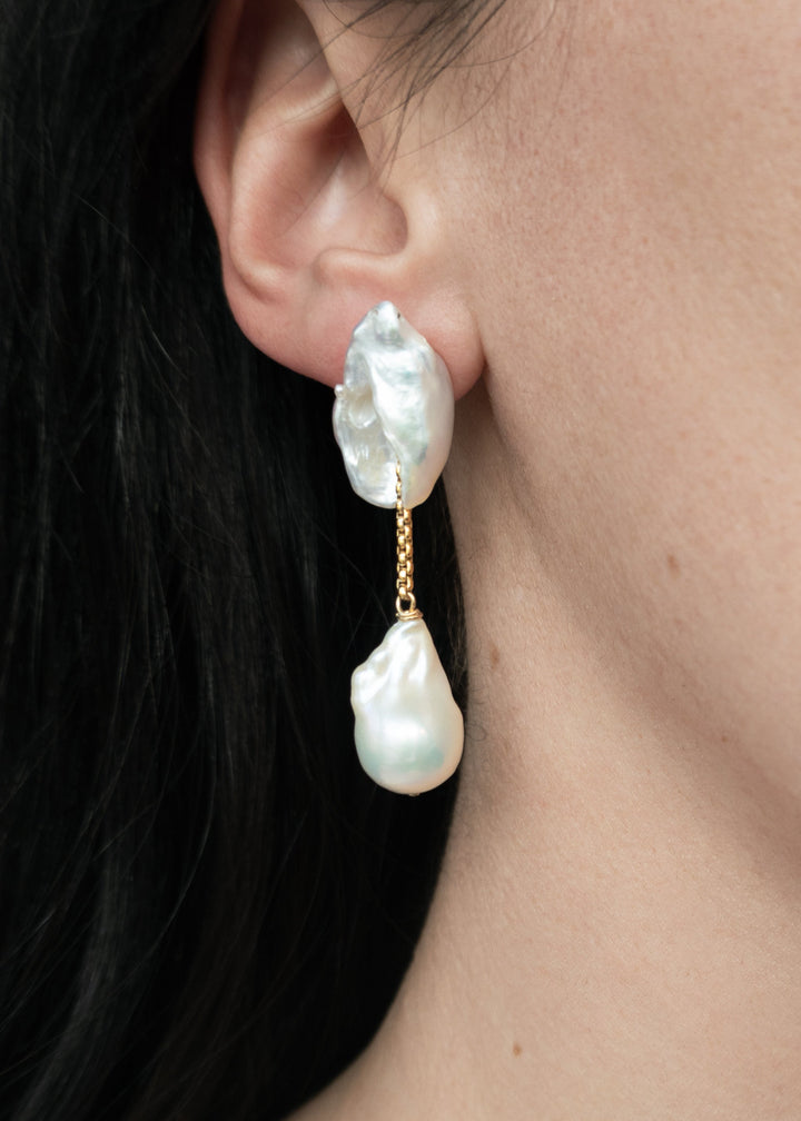 Dessa - These earrings feature two large keshi pearls shaped like conch shells, offering a unique and textured focal point. Suspended from a sleek round box chain, a large baroque pearl hangs at the end, creating a stunning contrast of organic shapes and