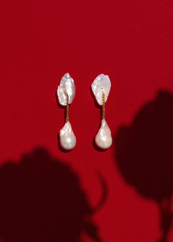 Dessa - These earrings feature two large keshi pearls shaped like conch shells, offering a unique and textured focal point. Suspended from a sleek round box chain, a large baroque pearl hangs at the end, creating a stunning contrast of organic shapes and