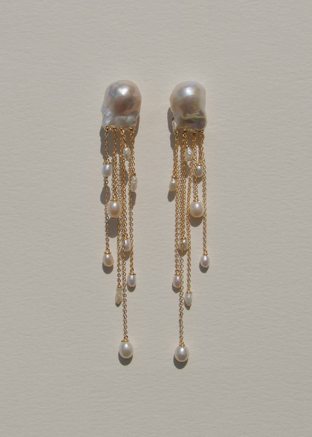 Gia - Like something drifting just beneath the surface, delicate, fluid, and quietly striking. Two baroque pearls anchor cascading chains of varied lengths, each adorned with luminous pearls in unexpected shapes. At four inches long, they move with ease a