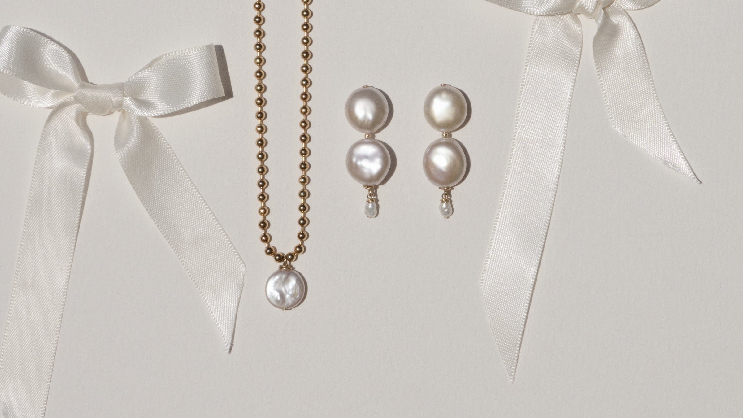 Pearl necklace and earrings with white ribbons on a light gray background