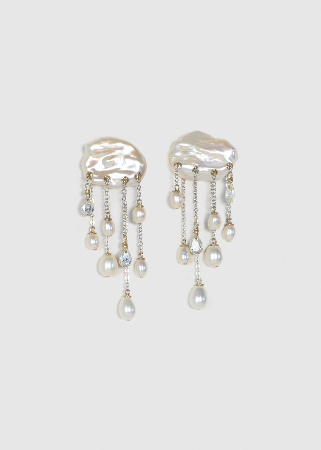 Pair of Halo 14k white gold earrings with white keshi pearl tops, cascading teardrop pearls and diamonds on a light background.