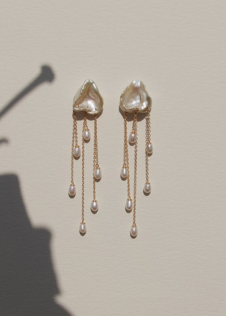 Inez - Two luminous keshi pearls anchor these earrings, imperfect in shape, yet perfectly matched. Their sculptural forms and 14k gold chains create a balanced silhouette that feels both refined and untamed. Delicate, dramatic, and made to frame the face