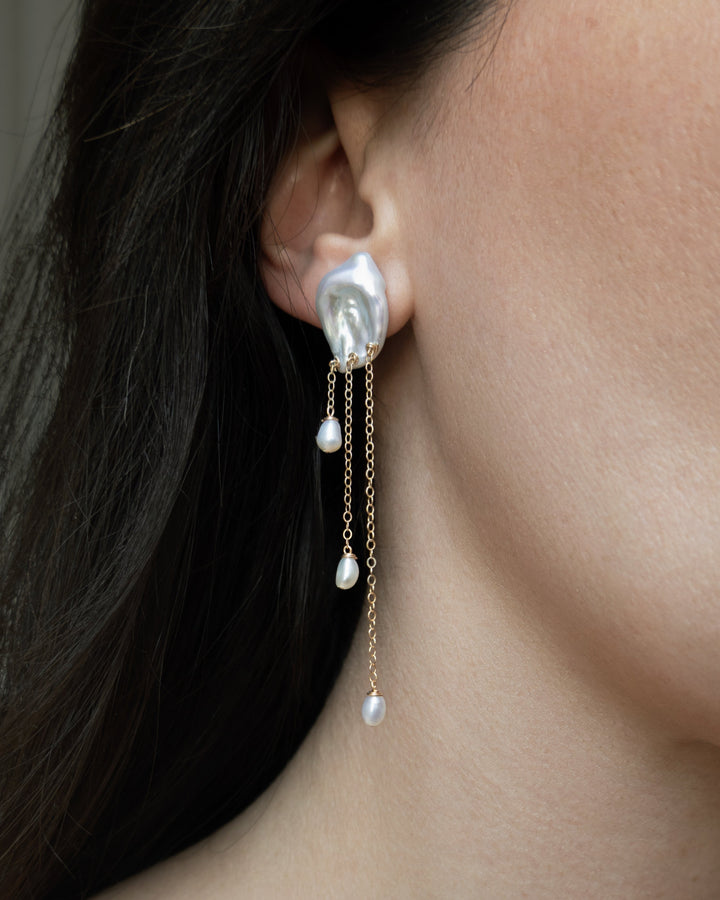 Laguna - These keshi pearls ripple like water touched by a falling drop soft, fluid, and full of light. Suspended below, three 14k gold chains fall at varying lengths, cascading like a quiet stream. Reflective and refined, they bring a sense of calm movem