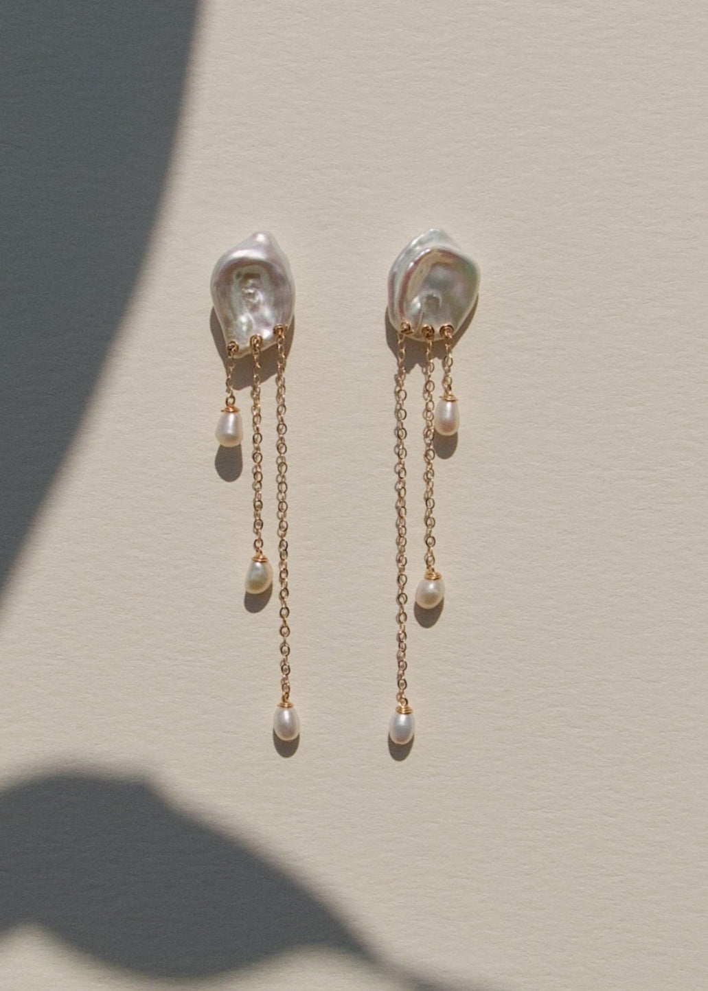 Laguna - These keshi pearls ripple like water touched by a falling drop soft, fluid, and full of light. Suspended below, three 14k gold chains fall at varying lengths, cascading like a quiet stream. Reflective and refined, they bring a sense of calm movem