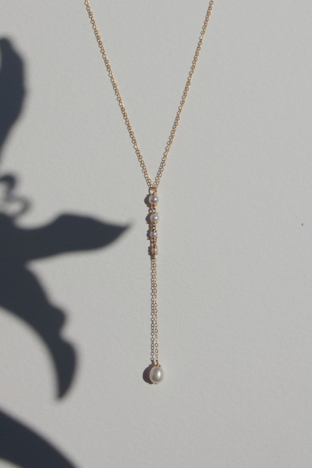 Lucine Necklace - A delicate choker lariat featuring four tiny seed pearls that taper from large to small, finished with a single teardrop pearl at the end. Crafted on a reflective chain, the Lucine balances elegance with an understated edge. 14K Gold-Fil