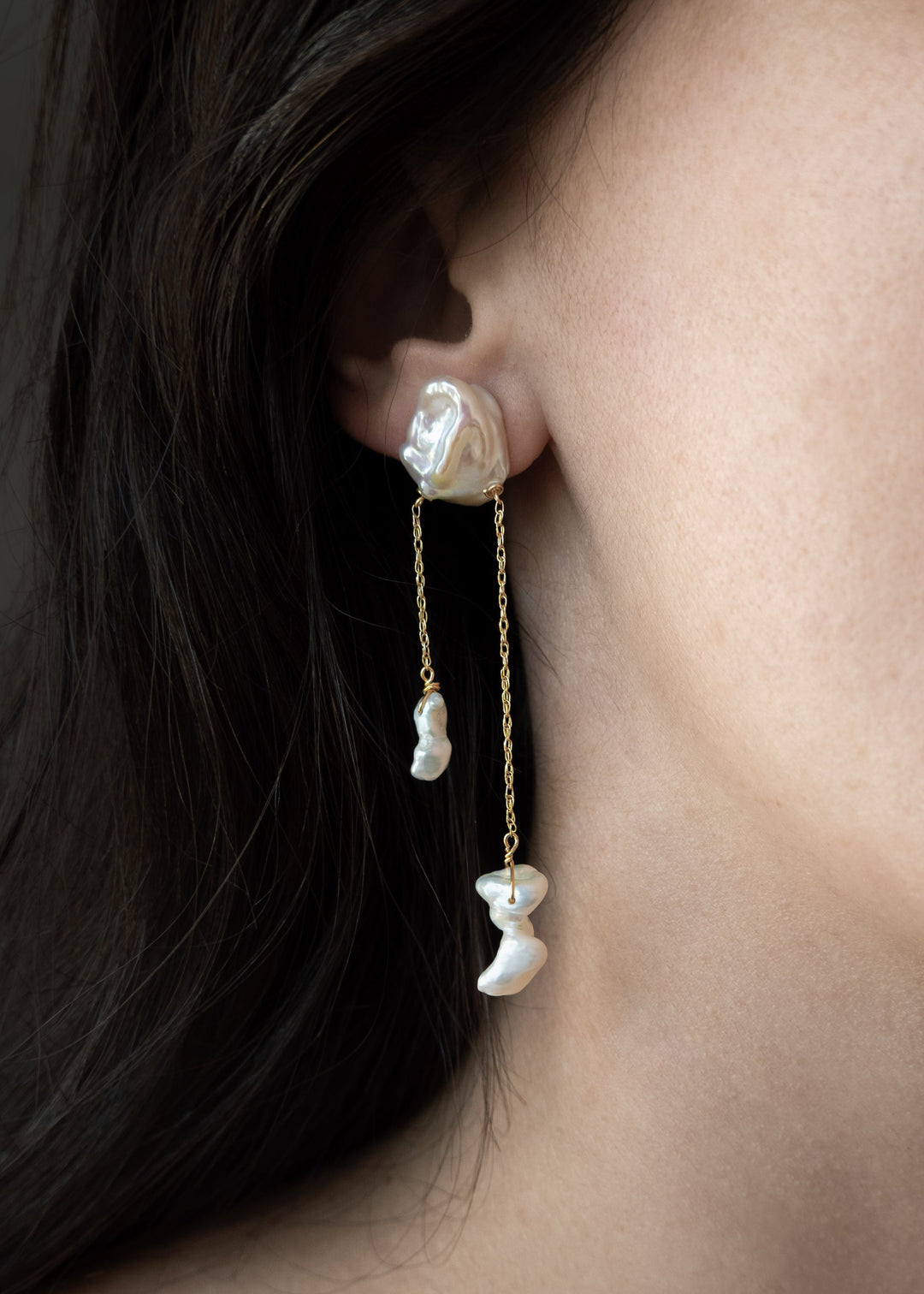 Close-up of a woman wearing pearl earrings with a dark background