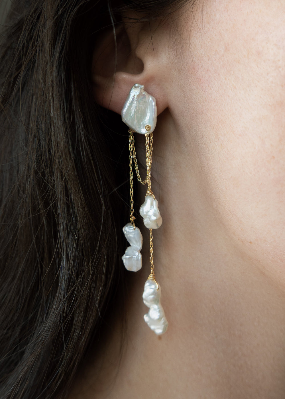 Close-up of a woman wearing pearl earrings with a neutral background