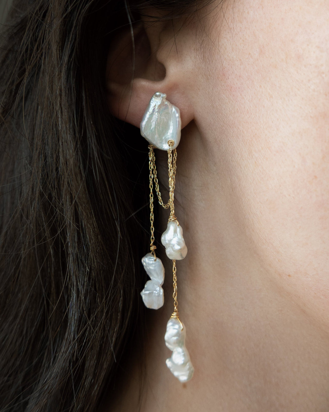 Close-up of a woman wearing pearl earrings with a neutral background