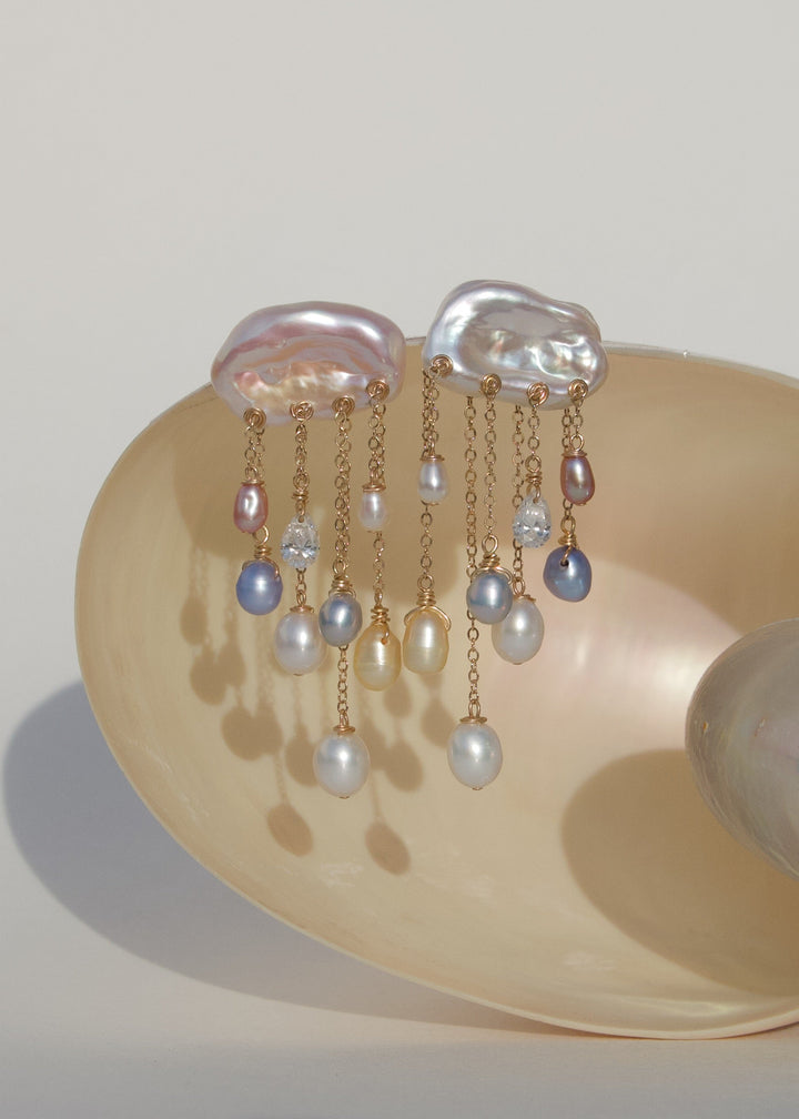 Moonlight pearl and diamond earrings displayed on a shell, with white keshi pearl tops and colorful teardrop pearls on 14k gold chains.