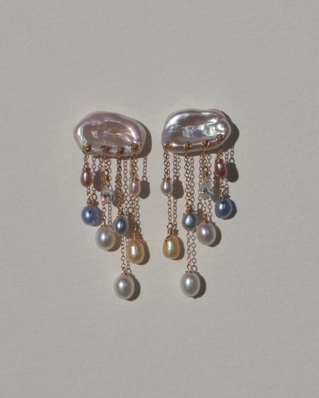 Front view of Moonlight 14k gold earrings with iridescent keshi pearl tops, multicolored teardrop pearls and diamonds against a neutral wall.