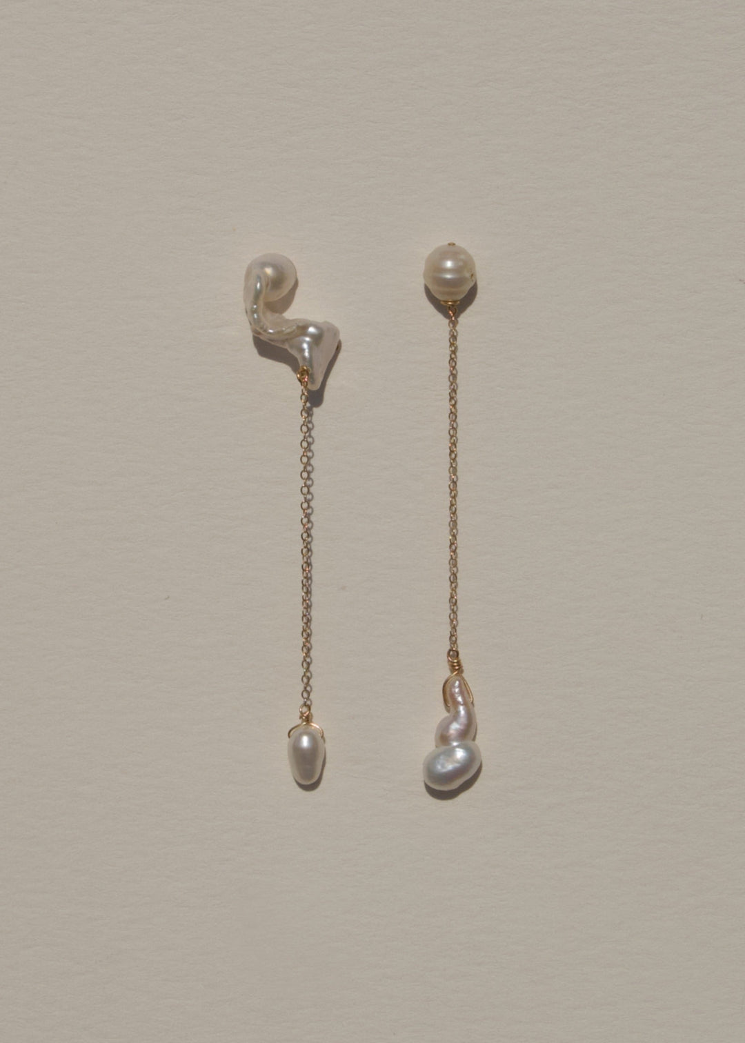 Nova - These asymmetrical earrings feature a crescent-shaped pearl on one side, evoking the delicate curve of the moon. Dainty chains hang from each end, with a teardrop pearl dangling at the bottom, creating an elegant design that balances softness and c