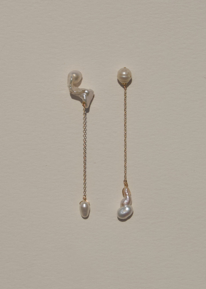 Nova - These asymmetrical earrings feature a crescent-shaped pearl on one side, evoking the delicate curve of the moon. Dainty chains hang from each end, with a teardrop pearl dangling at the bottom, creating an elegant design that balances softness and c