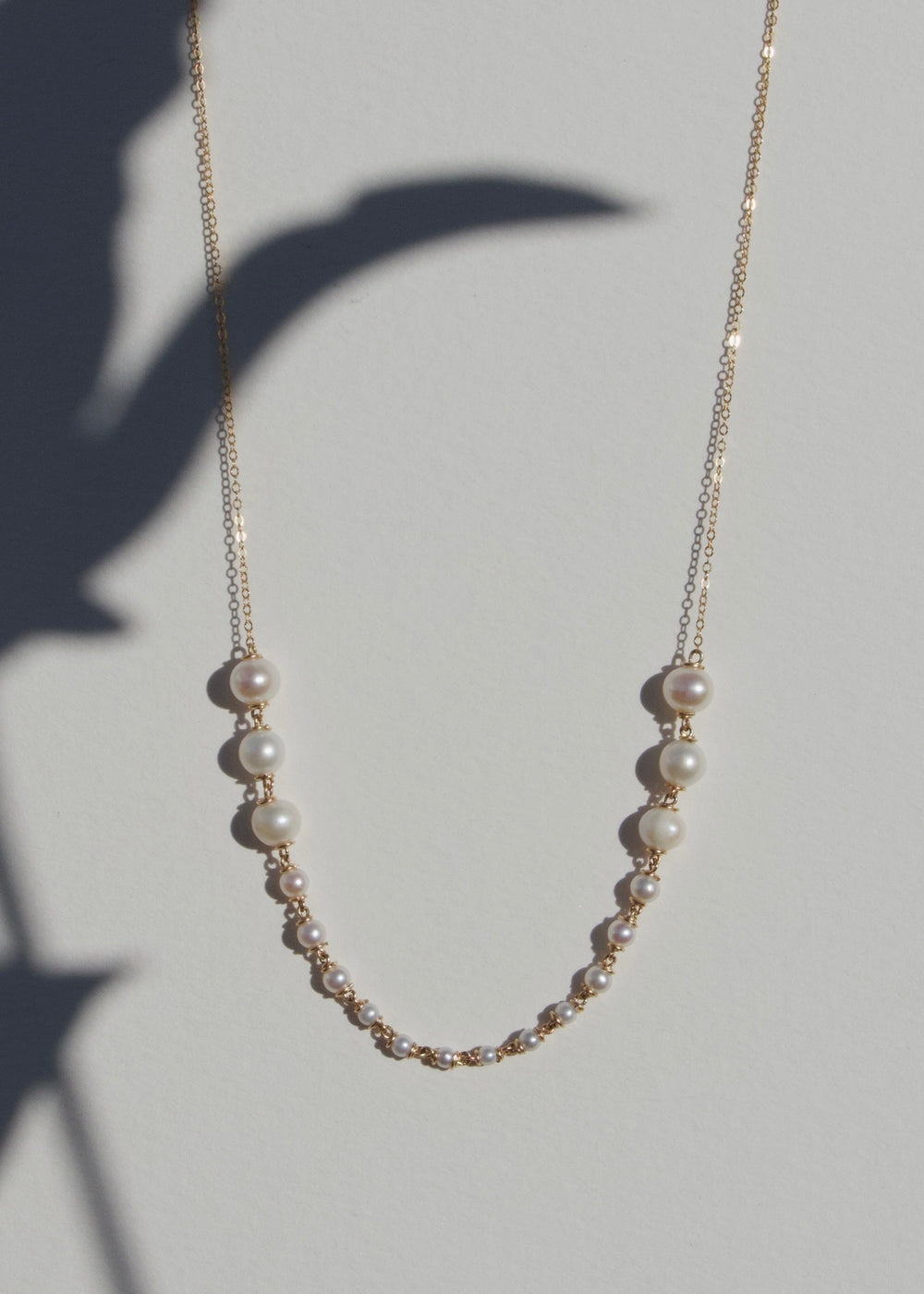 Odette Necklace draped on a beige wall with plant shadow