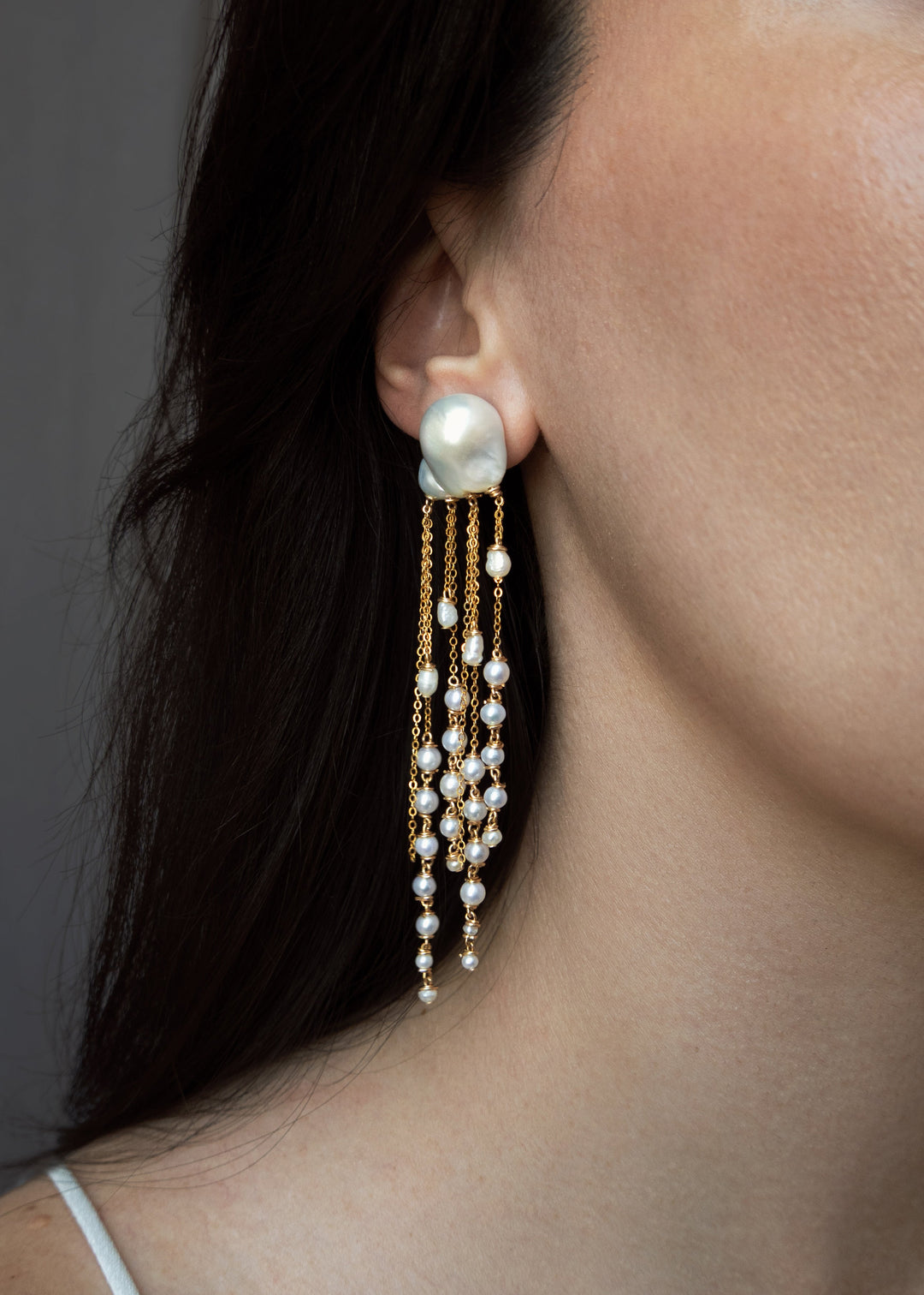 Close-up of a woman wearing pearl earrings with a neutral background