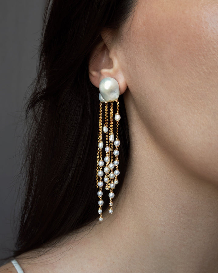 Close-up of a woman wearing pearl earrings with a neutral background
