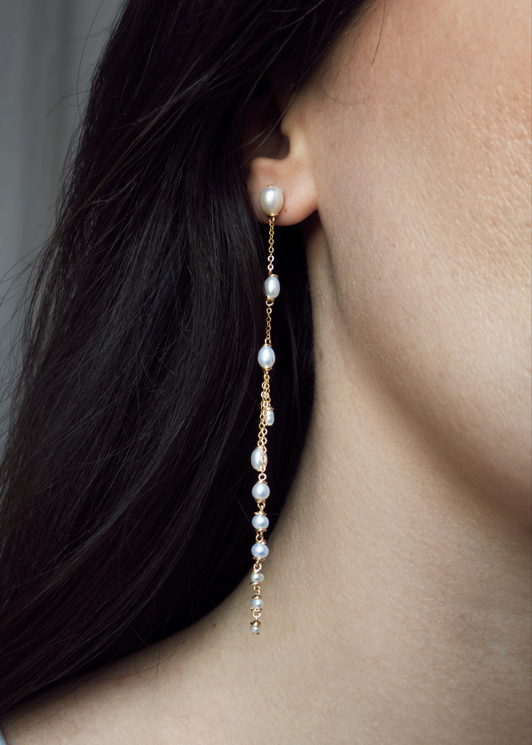 Close-up of a person wearing a delicate pearl earring against a neutral background
