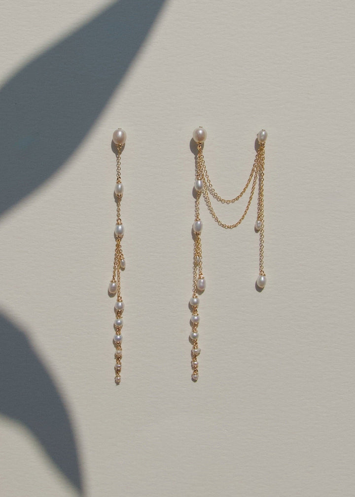 Pair of gold earrings with pearl-like beads on a light gray background