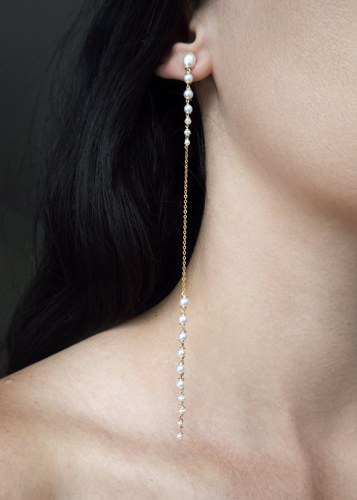 Posy - Minimal by design, but quietly captivating. These long earrings feature tapered strands of seed pearls, graduating from large to small, framing a single, reflective chain at the center. The effect is delicate yet striking, with just enough shimmer