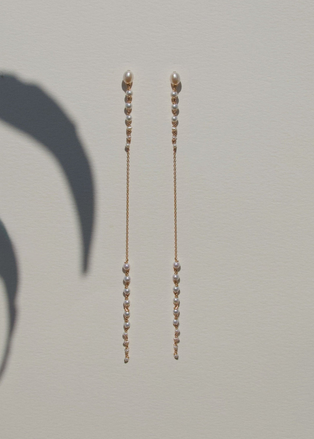 Posy - Minimal by design, but quietly captivating. These long earrings feature tapered strands of seed pearls, graduating from large to small, framing a single, reflective chain at the center. The effect is delicate yet striking, with just enough shimmer