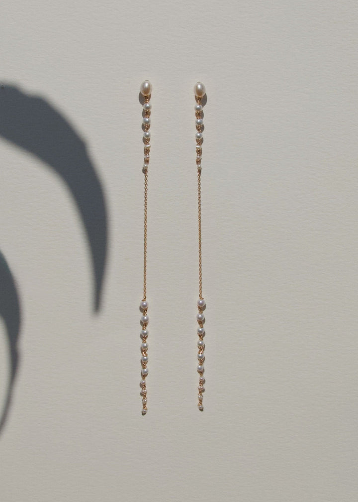 Posy - Minimal by design, but quietly captivating. These long earrings feature tapered strands of seed pearls, graduating from large to small, framing a single, reflective chain at the center. The effect is delicate yet striking, with just enough shimmer