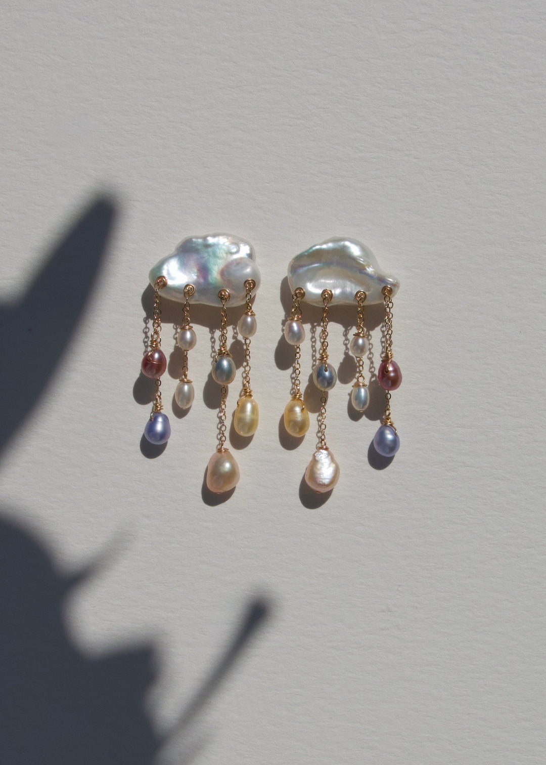 Rainstorm earrings on a light wall with plant shadow