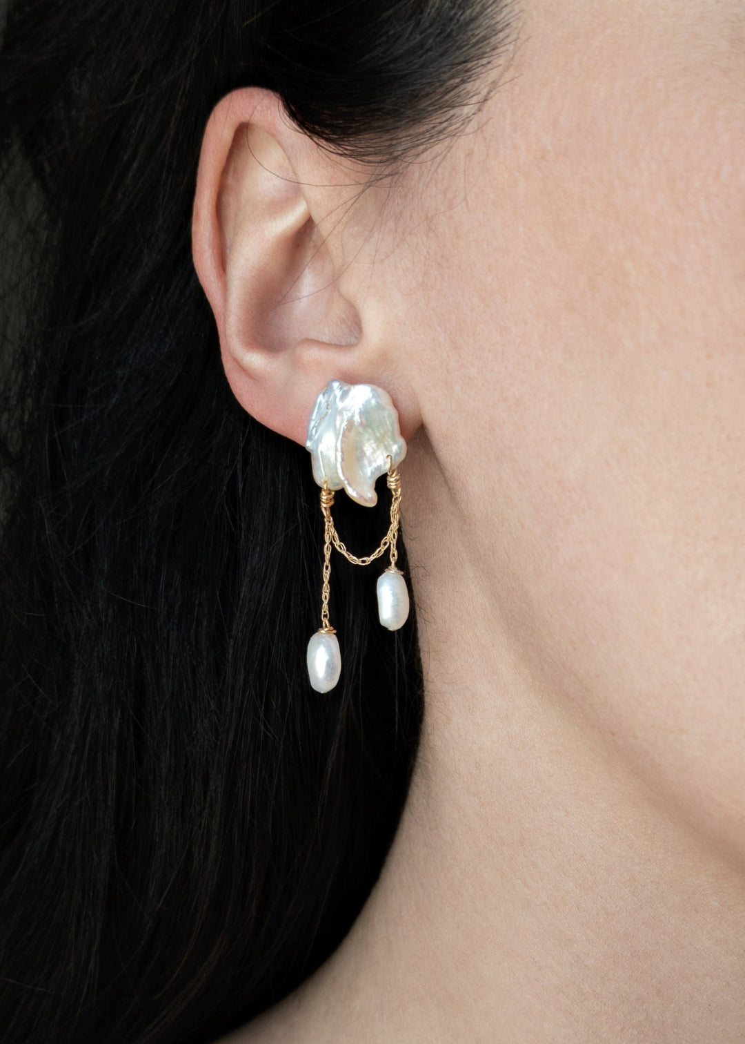 Rhea - These earrings feature two white keshi pearls, their asymmetrical design creating a striking yet playful balance of edge and elegance. Suspended from a substantial chain, pink baroque pearls dangle below, adding a sweet touch to the bold, modern si