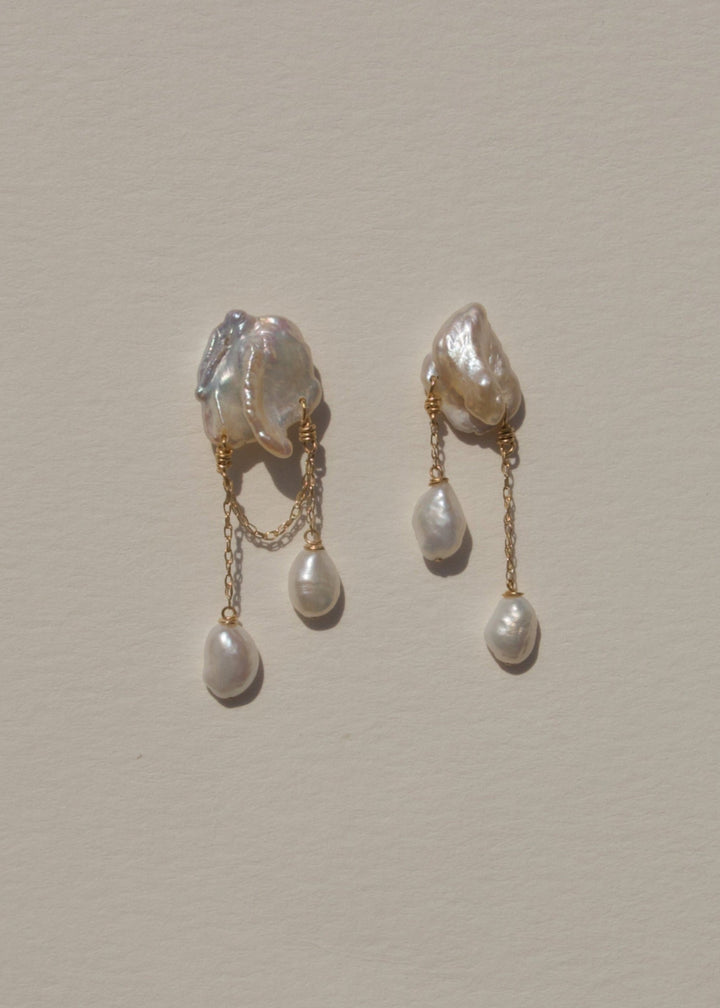 Rhea - These earrings feature two white keshi pearls, their asymmetrical design creating a striking yet playful balance of edge and elegance. Suspended from a substantial chain, pink baroque pearls dangle below, adding a sweet touch to the bold, modern si