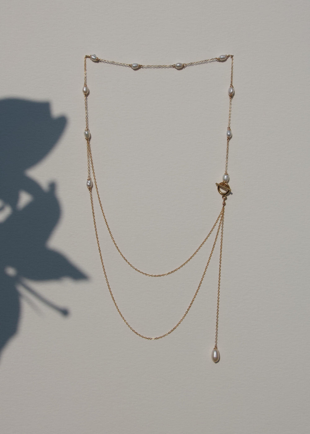 River Necklace draped on a beige wall with plant shadow