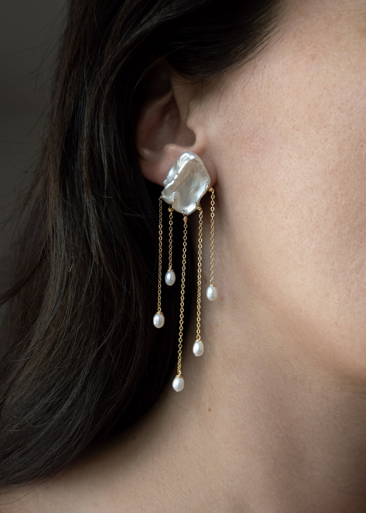 Sierra - Two one-of-a-kind keshi pearls serve as the focal point of these earrings, their organic shapes and colors radiating untamed beauty. Suspended from 14k gold chains, the asymmetrical design flows with effortless elegance, adding a touch of intrigu