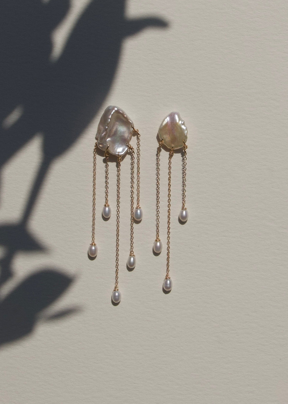 Sierra - Two one-of-a-kind keshi pearls serve as the focal point of these earrings, their organic shapes and colors radiating untamed beauty. Suspended from 14k gold chains, the asymmetrical design flows with effortless elegance, adding a touch of intrigu