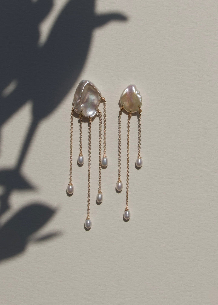 Sierra - Two one-of-a-kind keshi pearls serve as the focal point of these earrings, their organic shapes and colors radiating untamed beauty. Suspended from 14k gold chains, the asymmetrical design flows with effortless elegance, adding a touch of intrigu