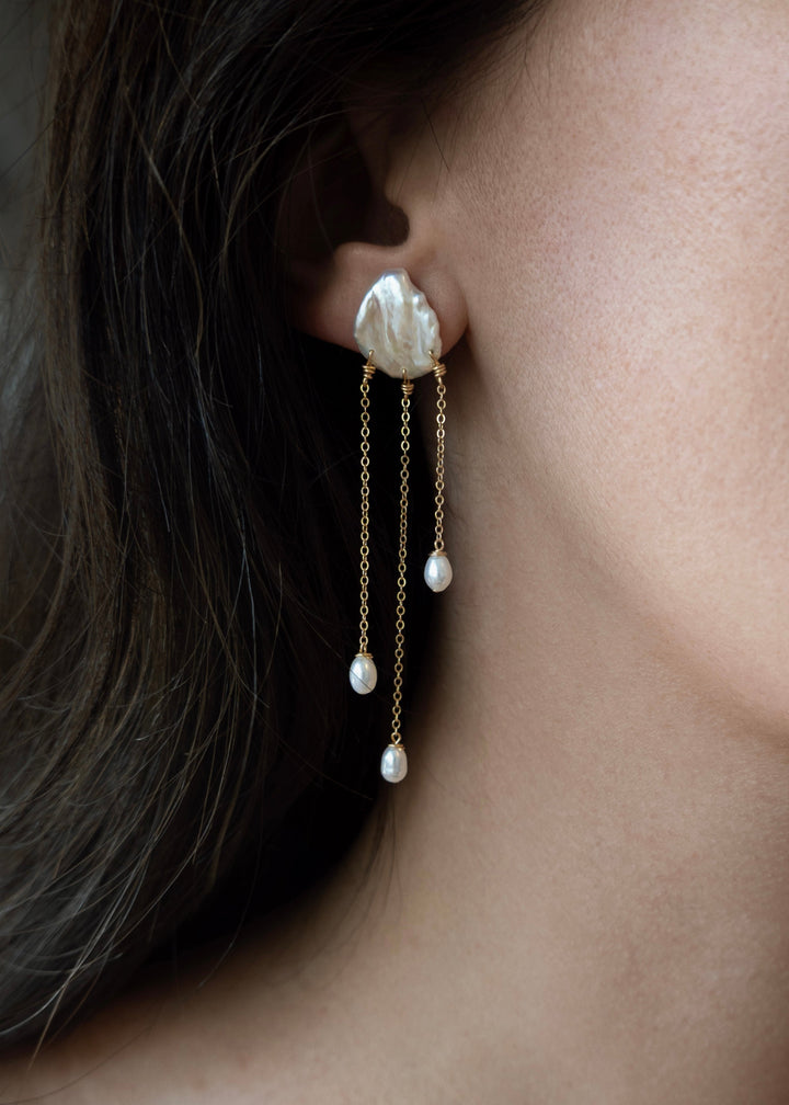 Sierra - Two one-of-a-kind keshi pearls serve as the focal point of these earrings, their organic shapes and colors radiating untamed beauty. Suspended from 14k gold chains, the asymmetrical design flows with effortless elegance, adding a touch of intrigu