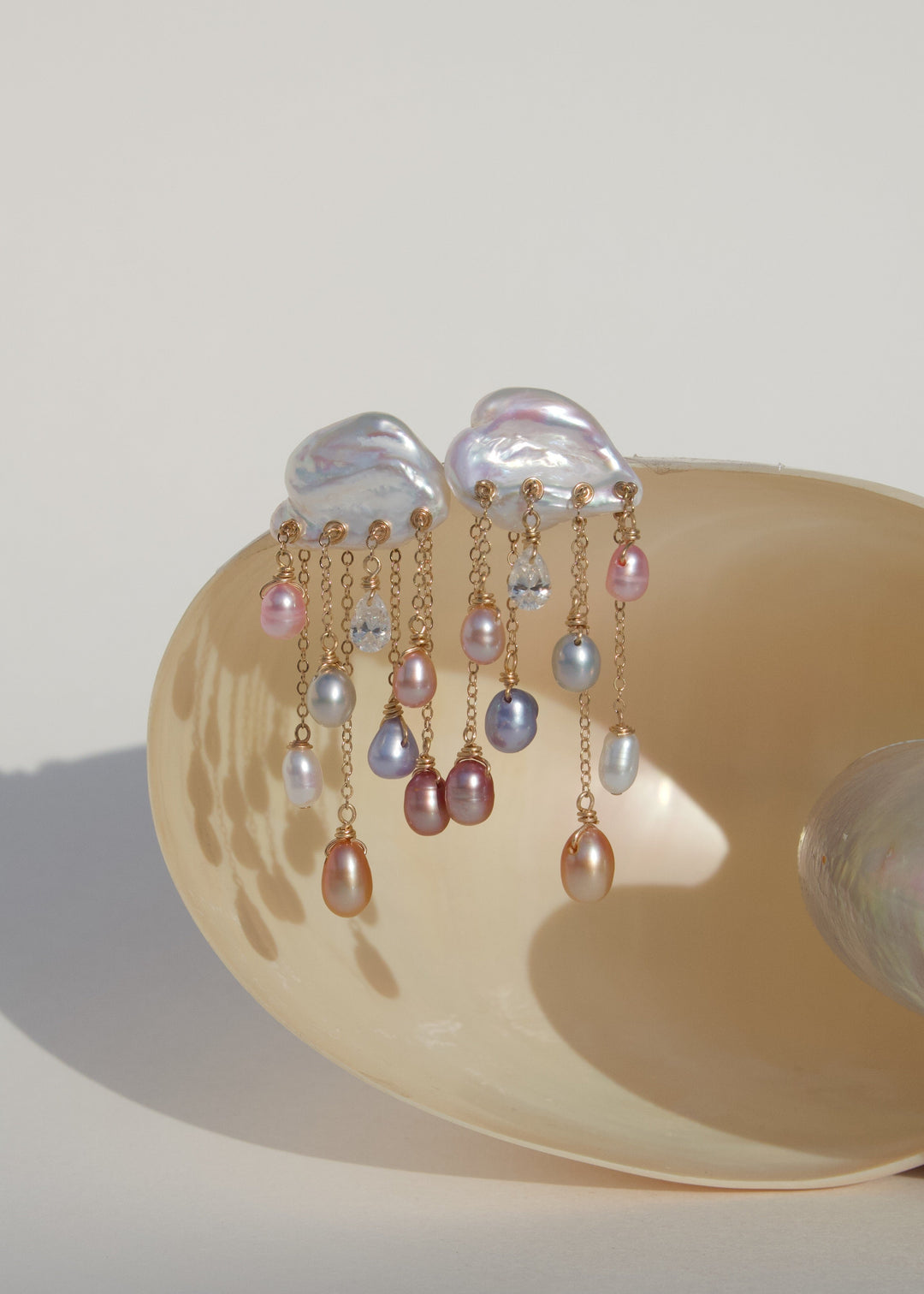Stardust 14k gold pearl and diamond earrings displayed on a shell, with white keshi pearl tops and cascading colorful teardrop pearls.