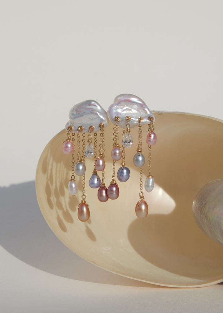 Stardust 14k gold pearl and diamond earrings displayed on a shell, with white keshi pearl tops and cascading colorful teardrop pearls.