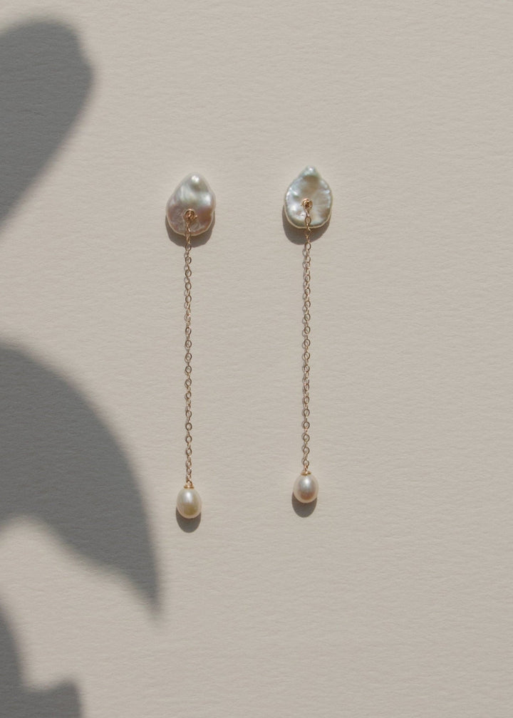 Viv - These earrings feature a single medium sized keshi pearl with a delicate 14k gold chain that falls gracefully below. At the end, a soft teardrop pearl adds a subtle glow and movement. Perfect for those who love something minimal yet distinct, especi