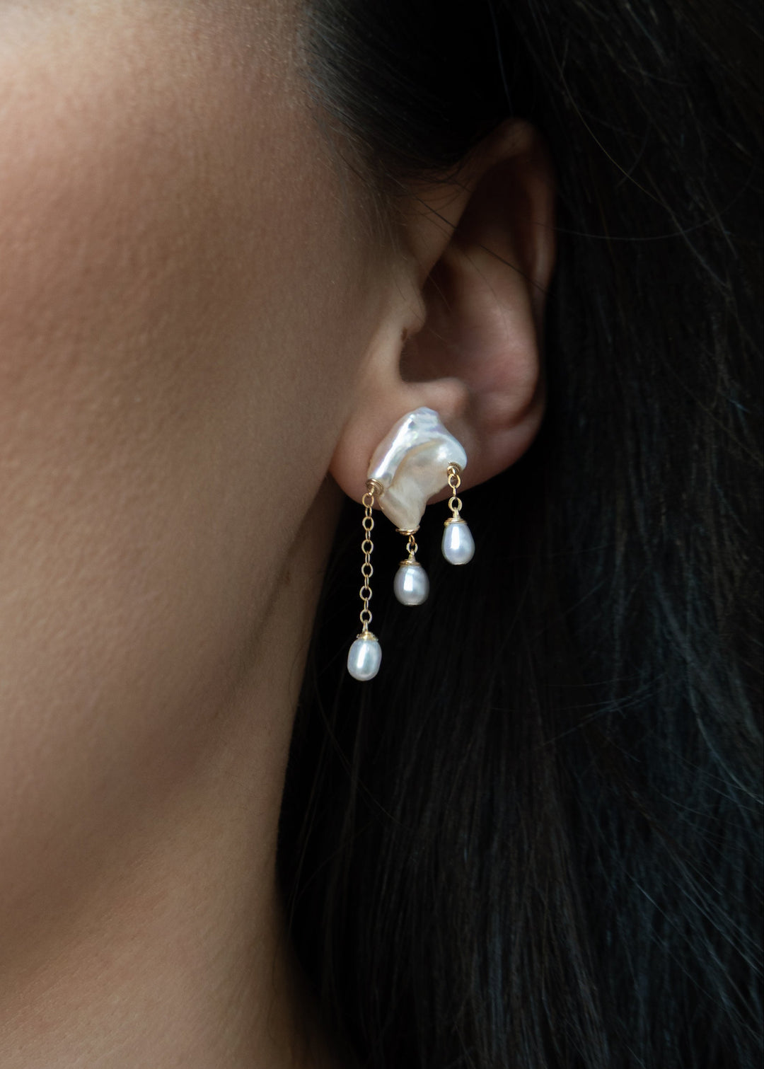 Close-up of a woman wearing a silver earring with dangling pearls.