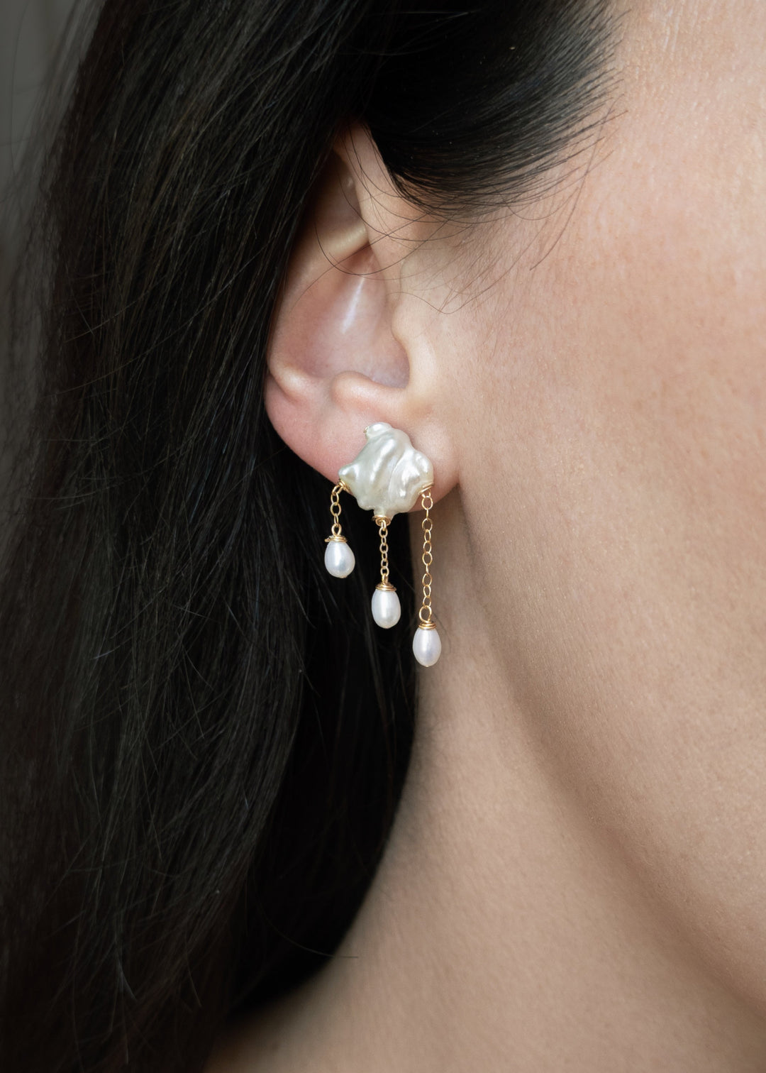 Close-up of a woman wearing pearl earrings with a neutral background